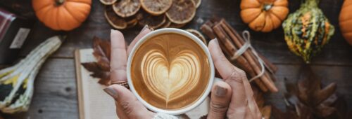 Jesienna kawa, kubek z gorącą kawą trzymany w dłoniach, w tle korzenne przyprawy i dynie, symbolika jesieni